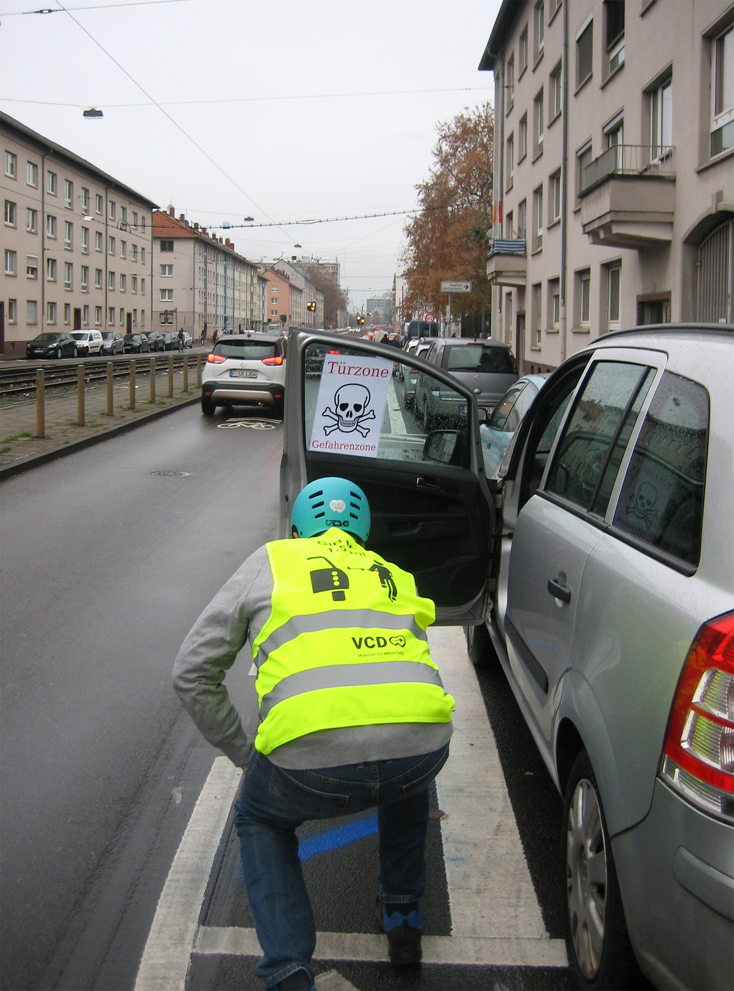 Ein Aktiver vom VCD (Verkehrs-Club Deutschland) bringt mit blauer Sprühkreide (nicht dauerhaft) Markierungen auf die Fläche, die die Radfahrer*innen nicht befahren sollen, um nicht in sich öffnende Türen zu fahrenFoto: Bertram Giebeler