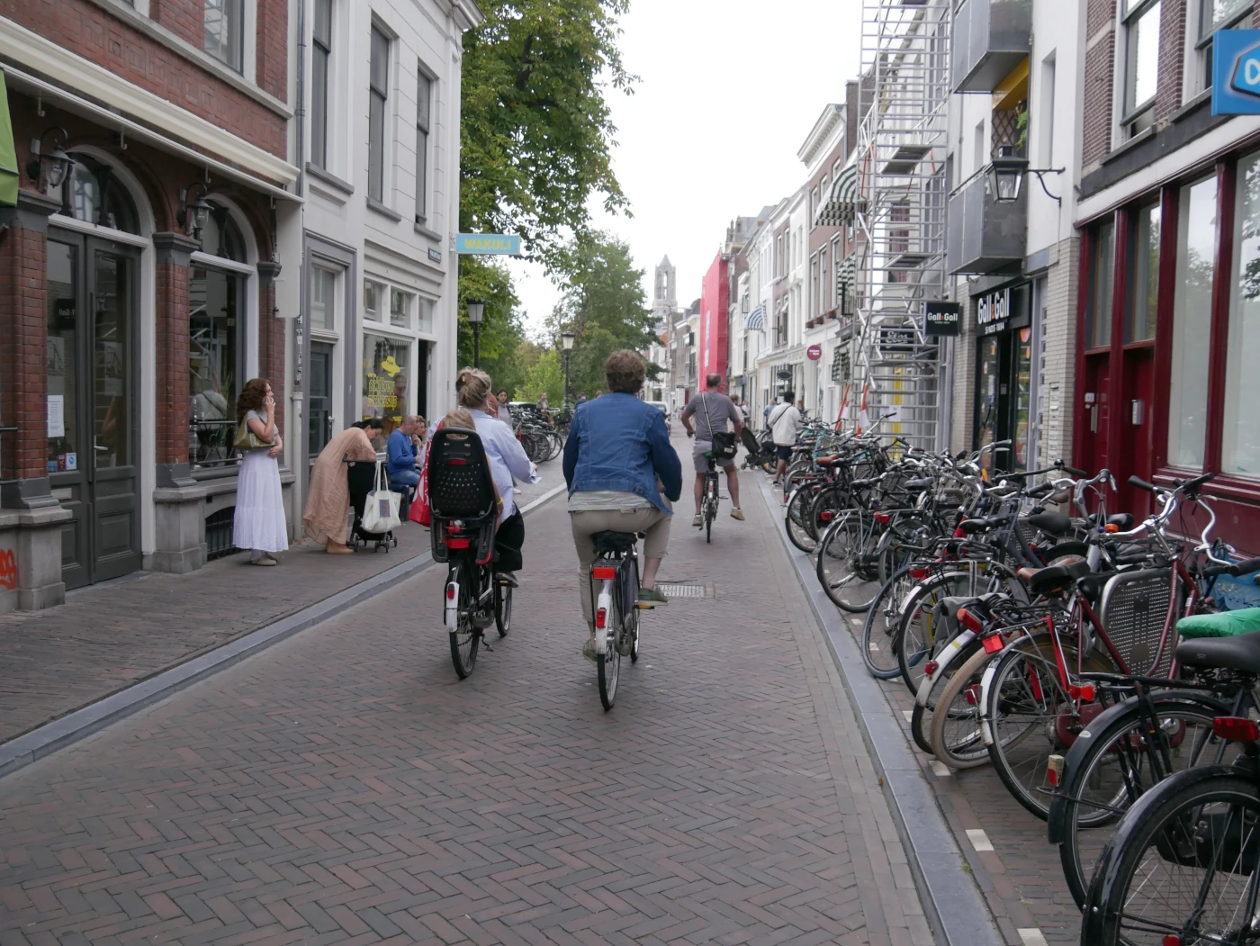 In einer niederländischen Stadt fahren Fahrradfahrer:innen. An der rechten Seite sind sehr viele Fahrräder geparkt