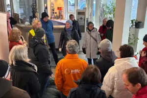 Eine Gruppe von Menschen hat sich in der Eingangshalle der Jugendherberge versammelt und hört der Klimastadträtin von Kassel, Simone Fedderke, zu