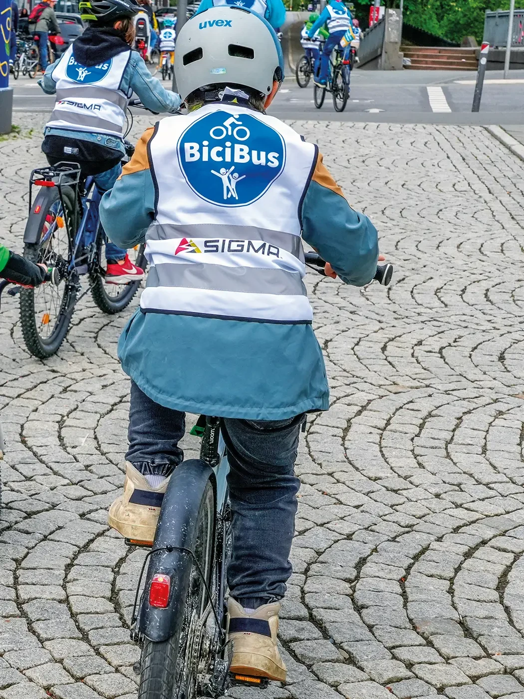 Ein Kind auf einem Fahrrad. Es trägt eine Jacke mit der Aufschrift „BiciBus“