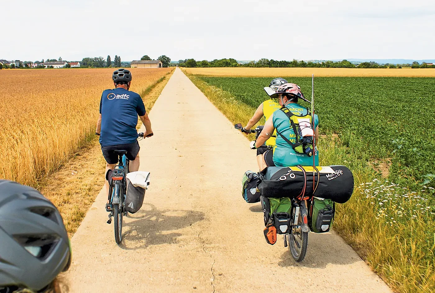 Drei Personen auf Fahrrädern fahren auf einem Radweg entlang